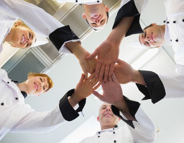 Chefs joining hands in a circle wearing uniforms in a kitchen